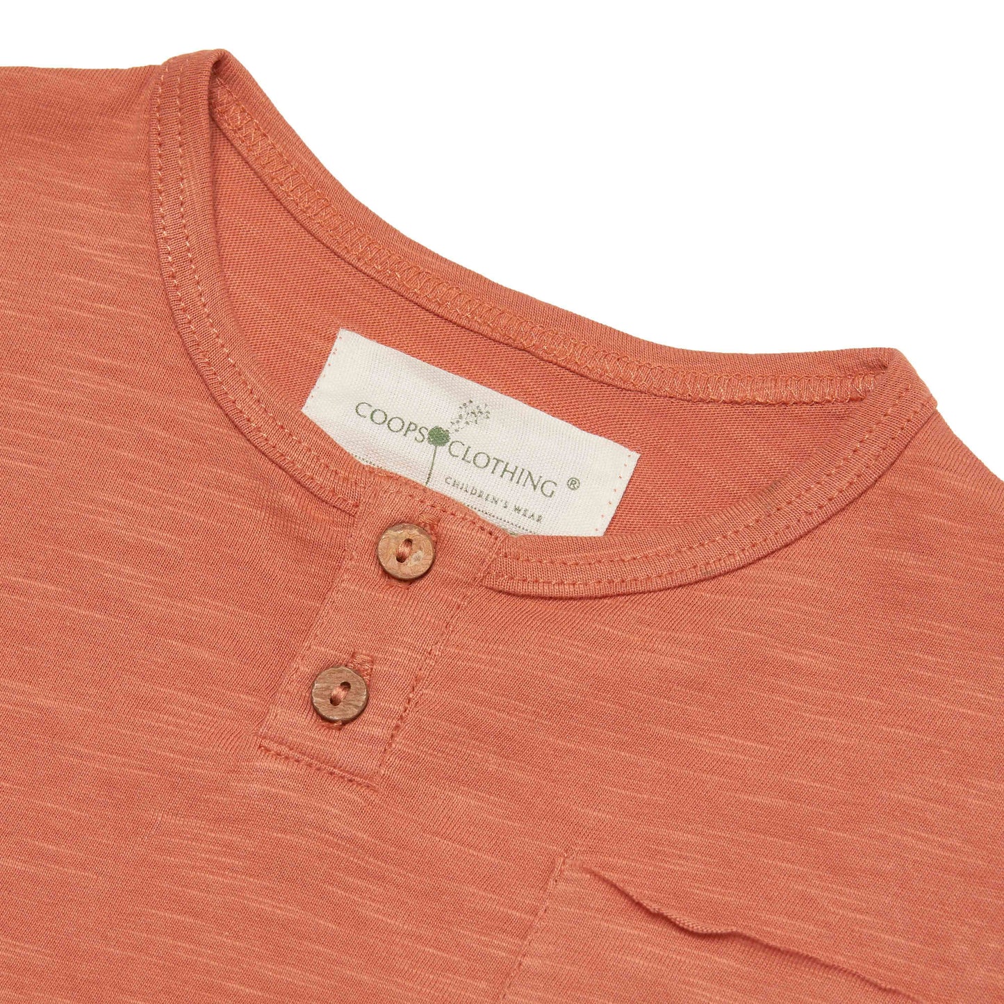 Close-up of a rust-colored shirt with a Coop's Clothing label on a white background with coconut shell buttons