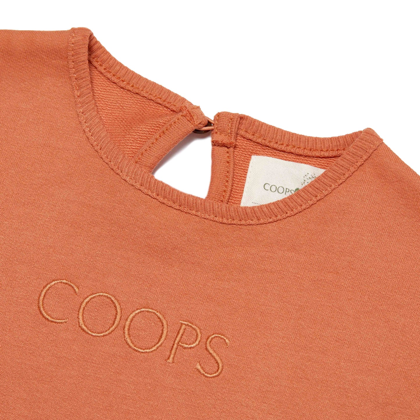Close-up of a rust-colored garment with 'COOPS' branding on a white background