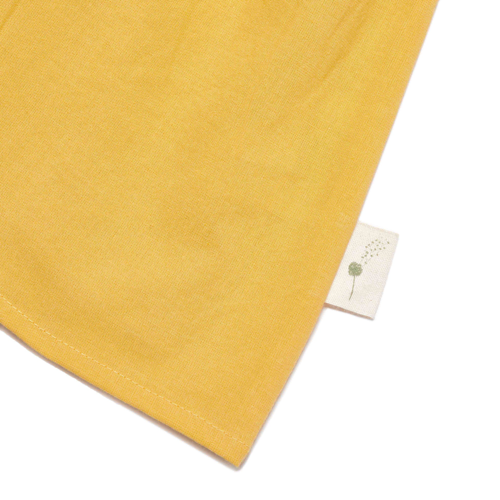 Close-up of a yellow fabric with a small white tag featuring a green leaf design on a white background.