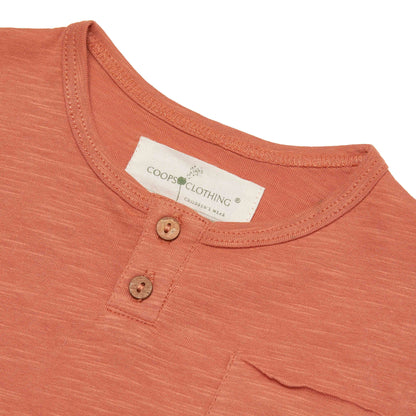 Close-up of a rust-colored shirt with a Coop's Clothing label on a white background with coconut shell buttons 