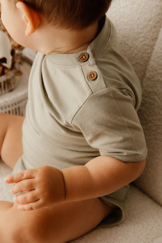 Child wearing a sage green organic cotton romper with coconut shell buttons 